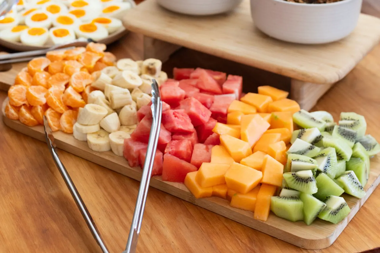 A breakfast board of melon, kiwi fruit, banana and orange, with yoghurt, granola and boiled eggs behind