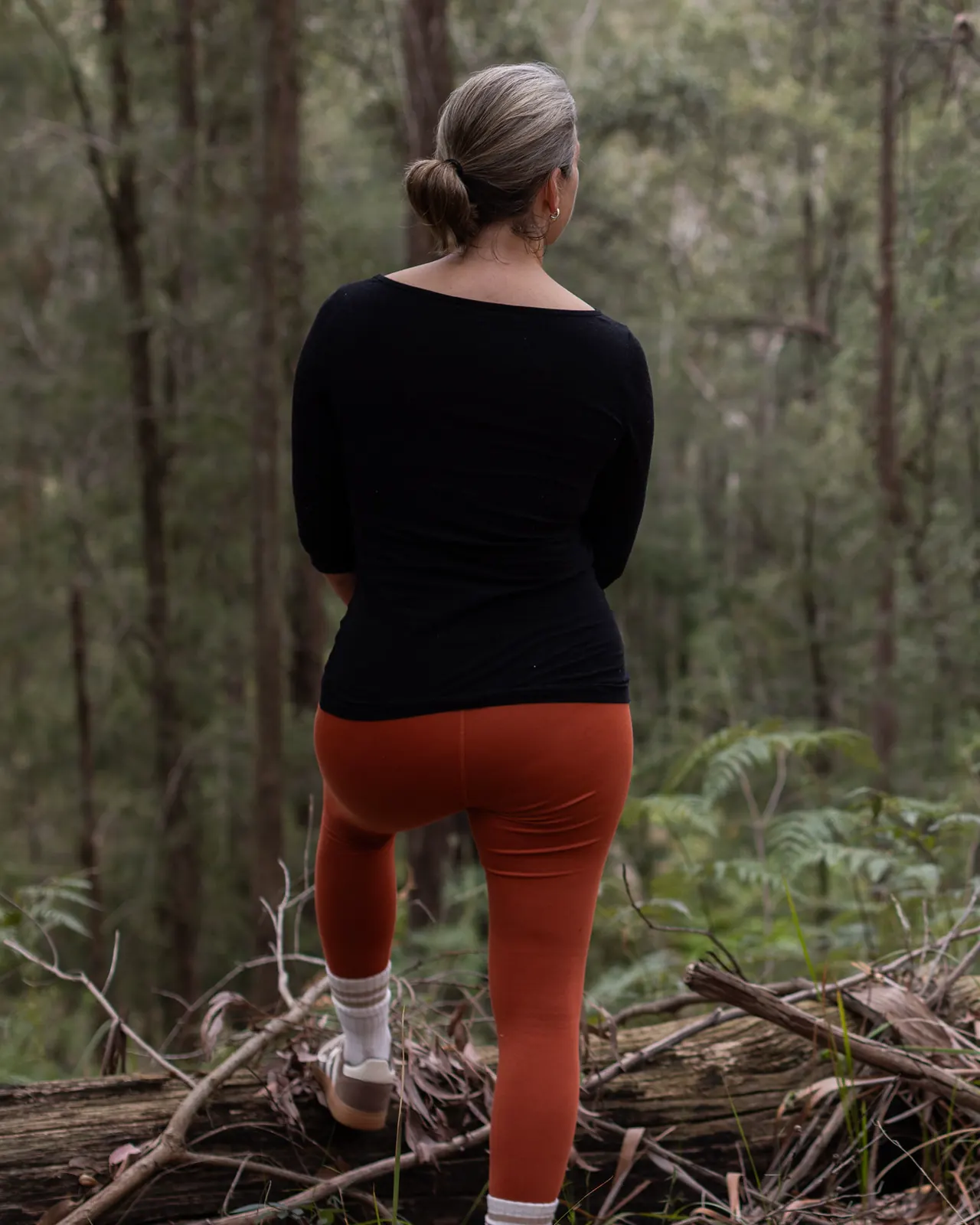 A guest steps up onto a fallen log and looks out into the bush
