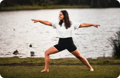 Natalie in a warrior pose on the grass beside a lake