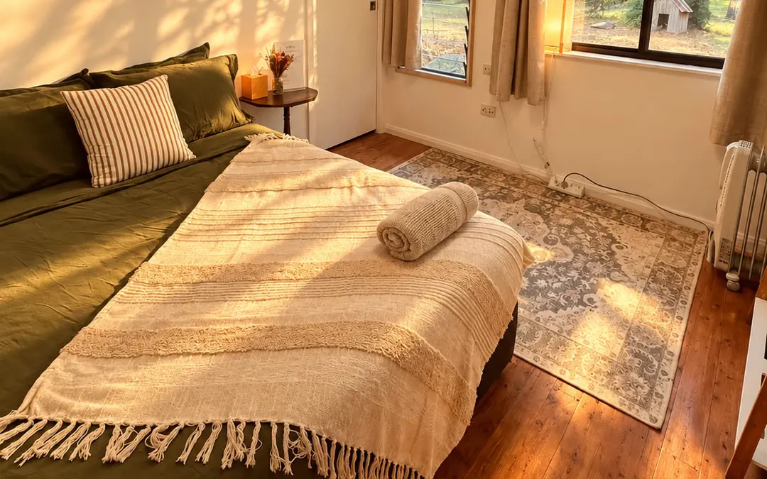 Woods: a double bed with dark green linen and a cream throw, a rug and windows onto tall trees