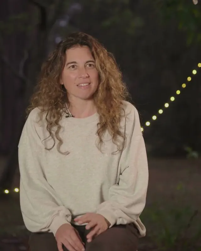 Rebecca, a guest, smiling, sitting outdoors at dusk with string lights behind her