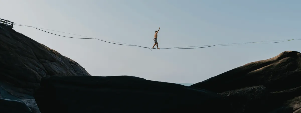 A person walking a slackline between two cliffs